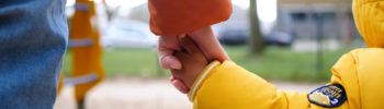 Erwachsene Hand hält Kinderhand von hinten fotografiert